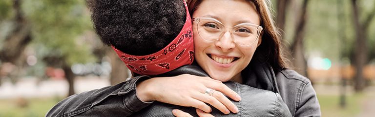 Happy girl looking at you while embracing her friend