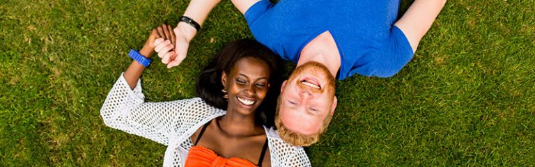 Multiracial Couple Laying on Grass Holding Hands