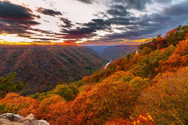 The sun rises over a picturesque landscape of a valley and lake, surrounded by lush green hills